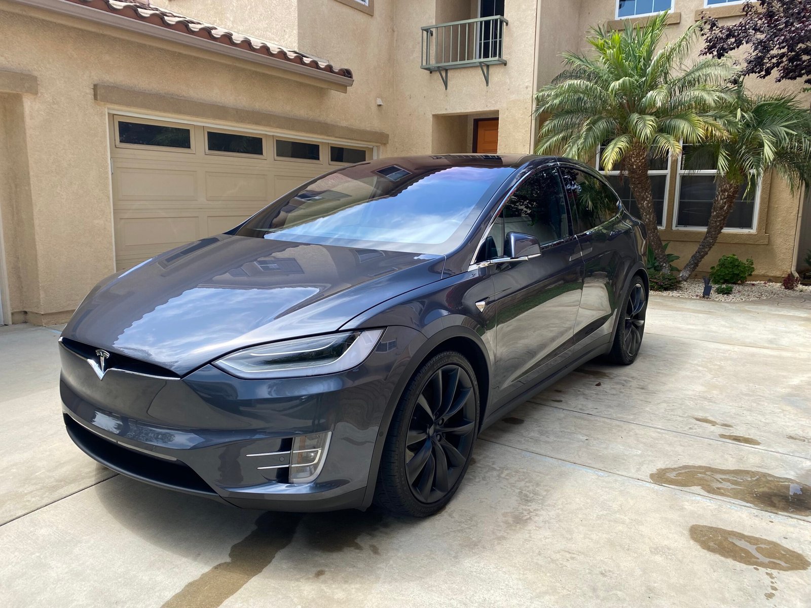 Dark gray Tesla sitting in driveway in front of a tan house